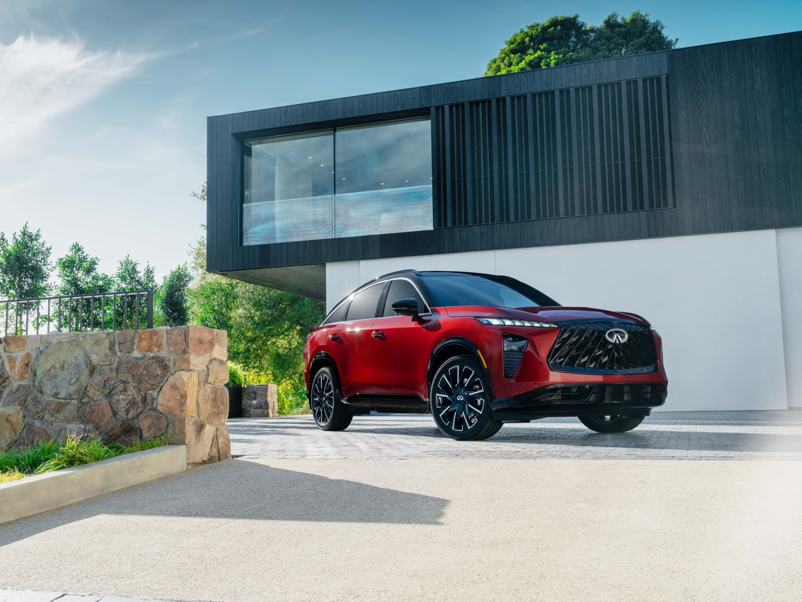2027 INFINITI QX65 in deep red with black contrast roof, parked at a modern Iowa home &mdash; front three-quarter view