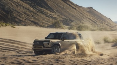 2026 Lexus GX 550 Overtrail+ in Earth paint, dust trailing as it crosses desert dunes