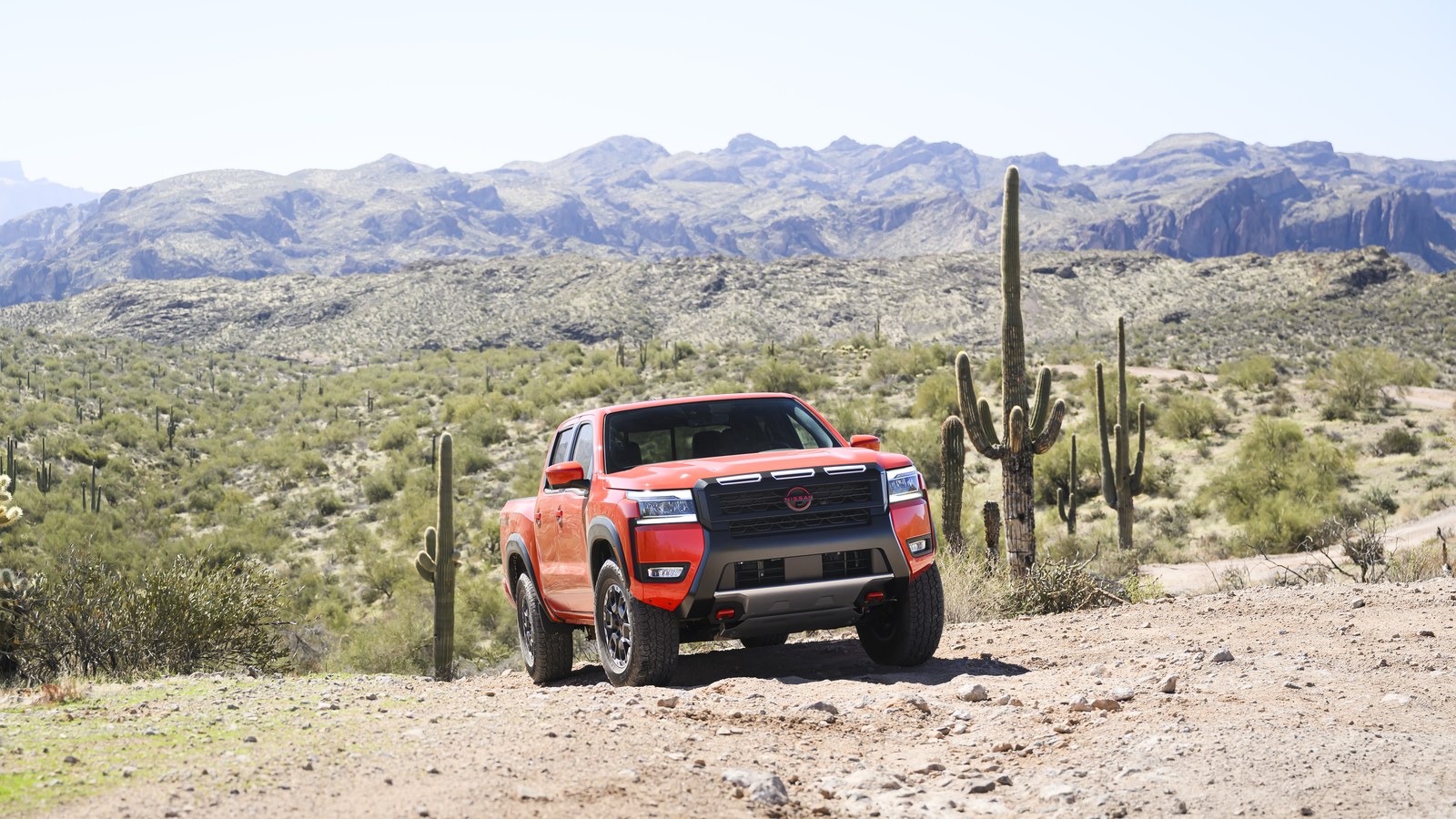 2027 Nissan Frontier PRO-4X in Afterburn Orange, front three-quarter view on a Sonoran desert backroad