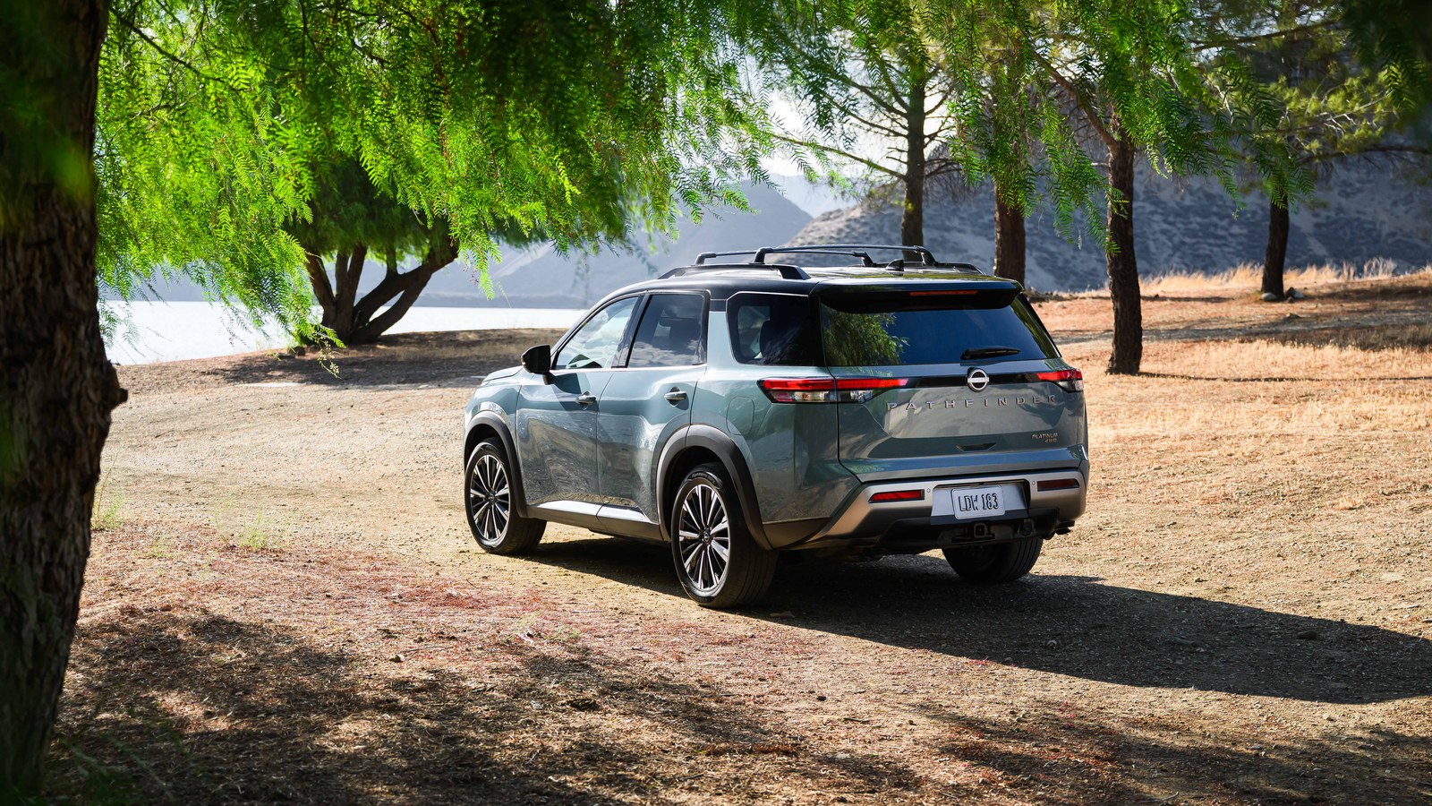 2026 Nissan Pathfinder Platinum in teal, rear three-quarter view at golden hour with lakeside trees